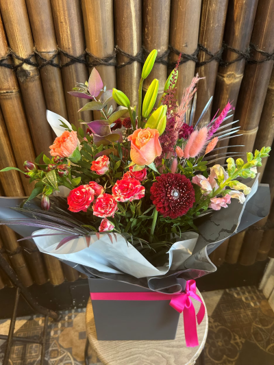 Blushing Embrace - This tender bouquet celebrates pinks in every shade, from gentle pastel blush to vibrant hot pink, softened by pretty peach and burgundy accents and delicate hints of green foliage.