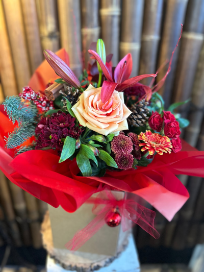 Fire & Chesnut - A bold, rustic arrangement with reds, glowing oranges, and earthy browns. May feature red lily, Xmas cones, red rose, orange spray rose, red and brown santini, alstroemeria, hypericum, Christmas pic, red birch, and festive wrappings. Flowers may vary but the design and value are always maintained.